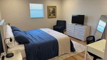 A bedroom with a bed, dresser, chair, TV, and ceiling fan.