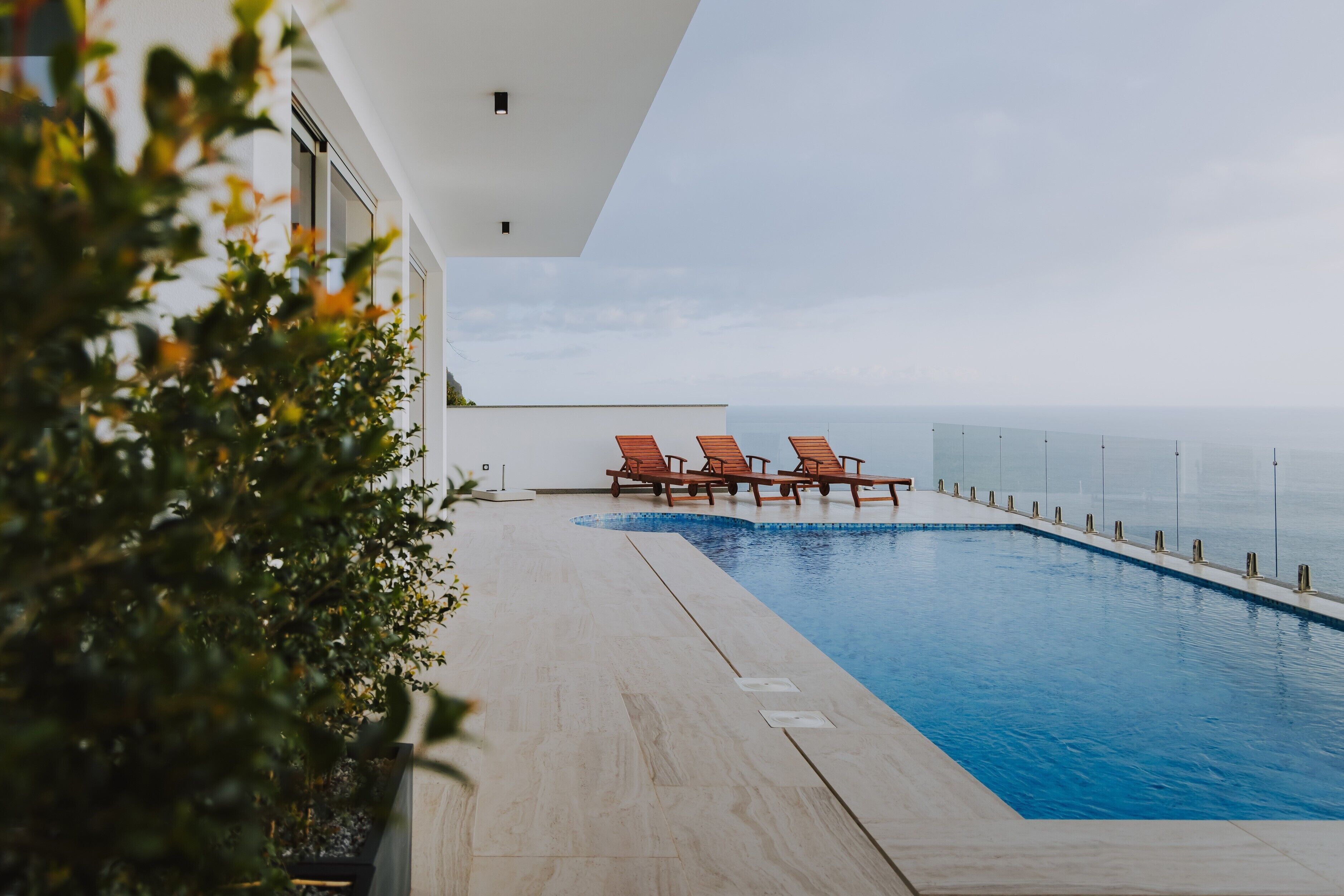 A swimming pool with lounge chairs, a clear view of the ocean, and a modern building with large windows.