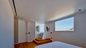 Un dormitorio moderno con una cama grande, vistas al mar y una escalera que conduce a un espacio exterior.
