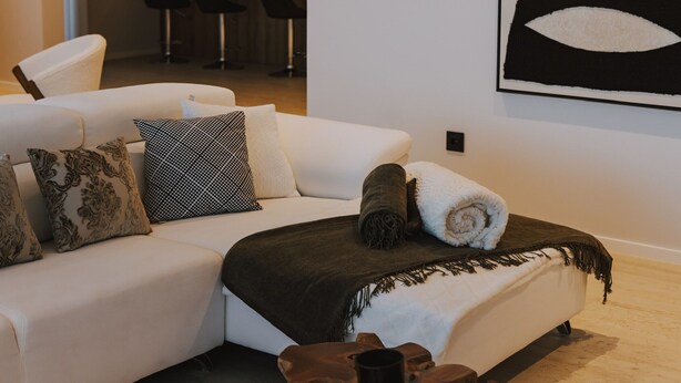 Una sala moderna con un sofá blanco, cojines estampados, una toalla enrollada y una mesa de centro de madera.