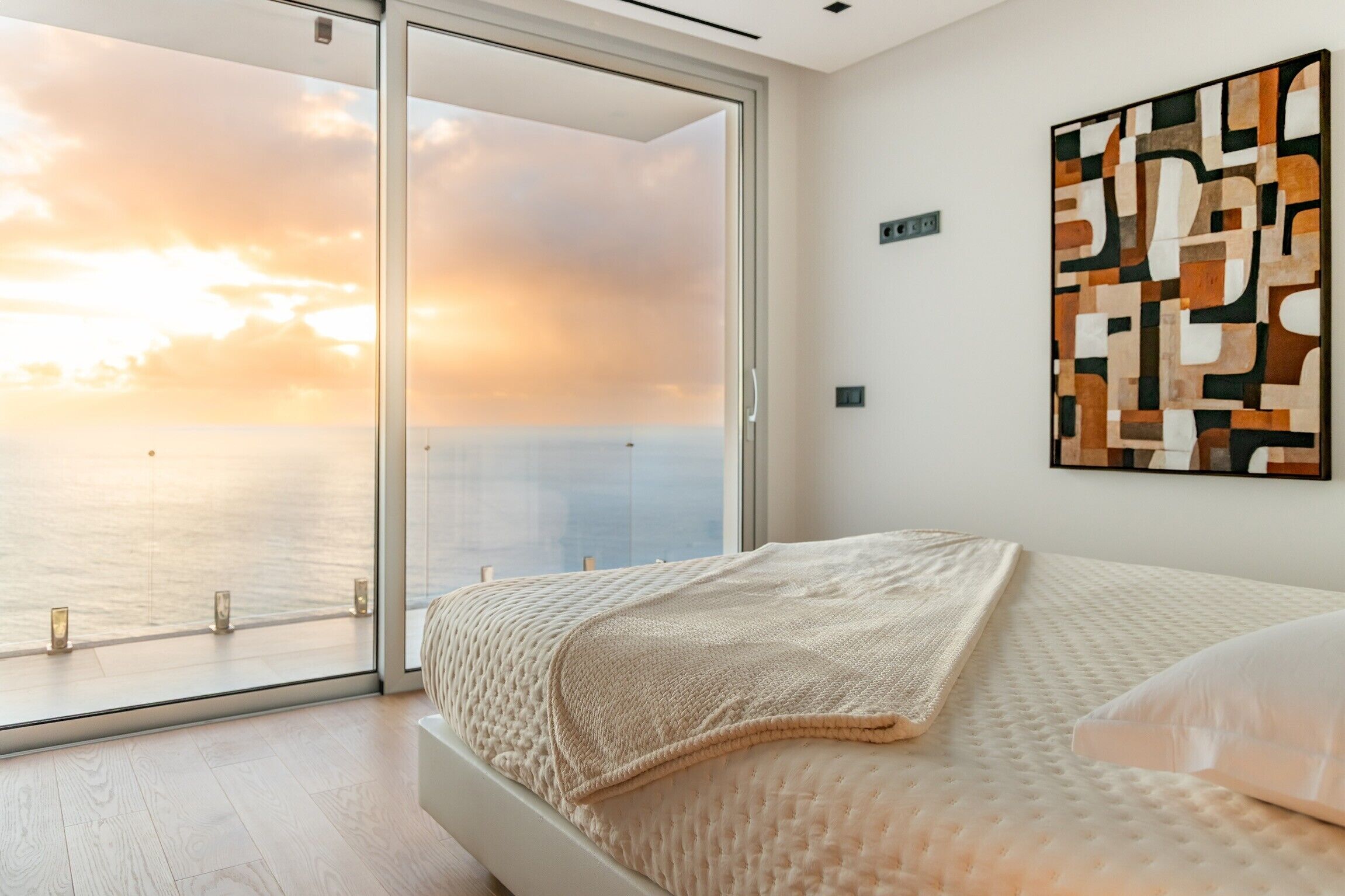 Ein Schlafzimmer mit großem Fenster, einem Bett mit strukturierter Decke und einem abstrakten Kunstwerk an der Wand.