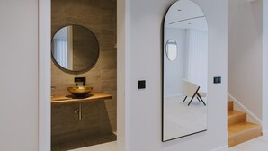Un baño moderno con un espejo redondo, un tocador de madera y un espejo arqueado grande.