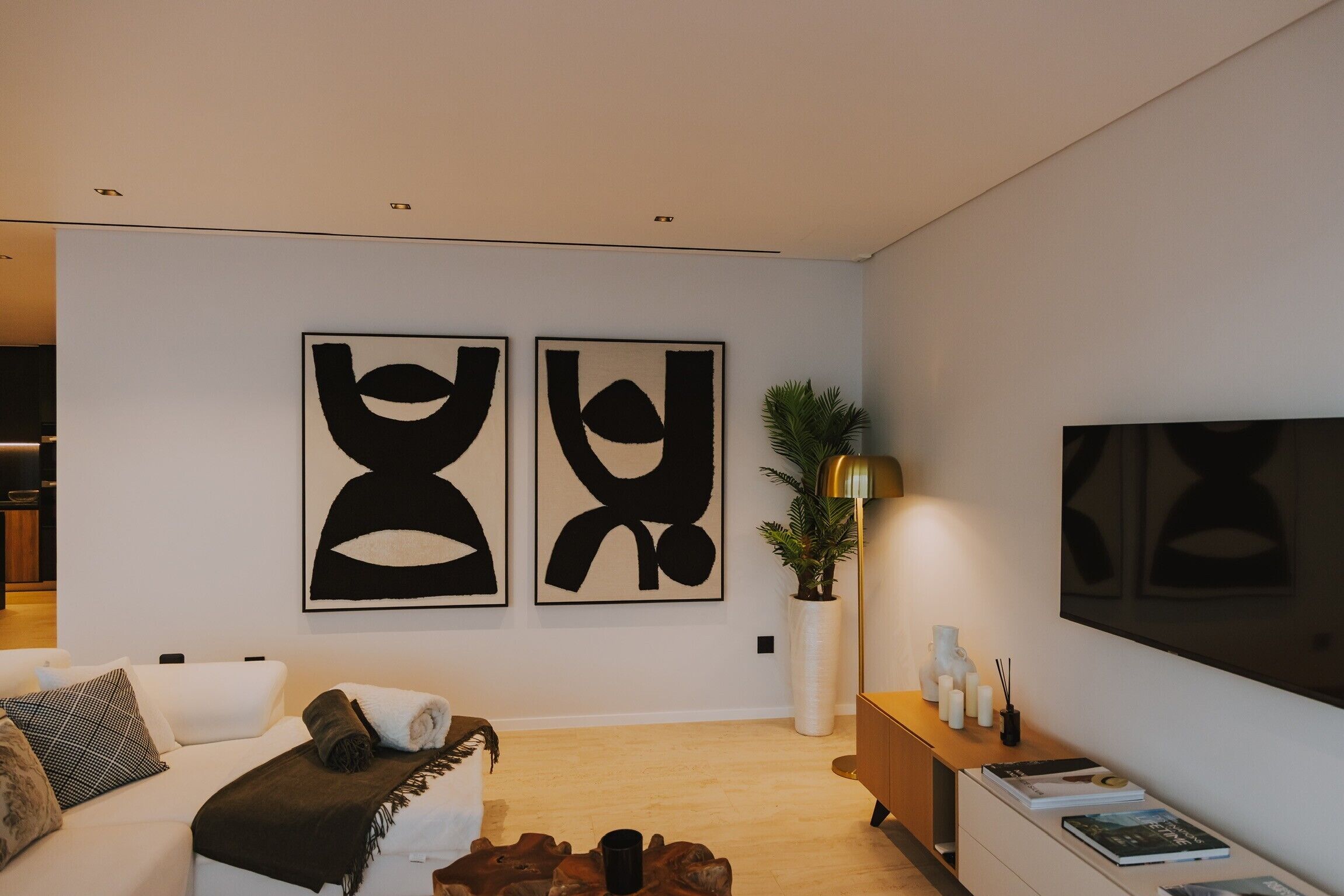 Un salon moderne avec un canapé, une table basse, une plante et deux tableaux abstraits accrochés au mur.