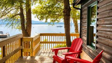 Une terrasse en bois avec des fauteuils Adirondack rouges, un chalet en bois et une vue sur le lac.