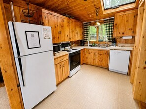 A compact kitchen with wooden cabinets, a white refrigerator, a stove, and a dishwasher.