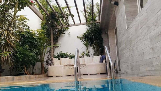 An indoor swimming pool with a glass ceiling, a white sofa, and various plants.