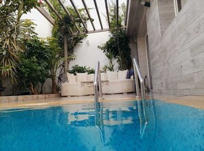 An indoor swimming pool with a glass ceiling, a white sofa, and various plants.