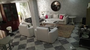 A living room with a sofa set, a coffee table, a round mirror, and a dining area with a table and chairs.
