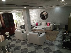 A living room with a sofa set, a coffee table, a round mirror, and a dining area with a table and chairs. - Modern Private Suite with Pool, Kitchen & Ensuite (Khémisset)