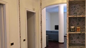 Una habitación con un espejo grande, un sofá azul, piso de madera y una estantería con estampado floral.