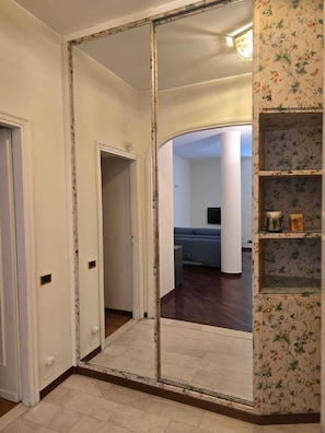 Ein Zimmer mit einem großen Spiegel, einem blauen Sofa, einem Holzboden und einem mit Blumenmustern versehenen Regal.