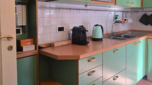 Una cocina con gabinetes verdes, microondas, hervidor de agua y cafetera.