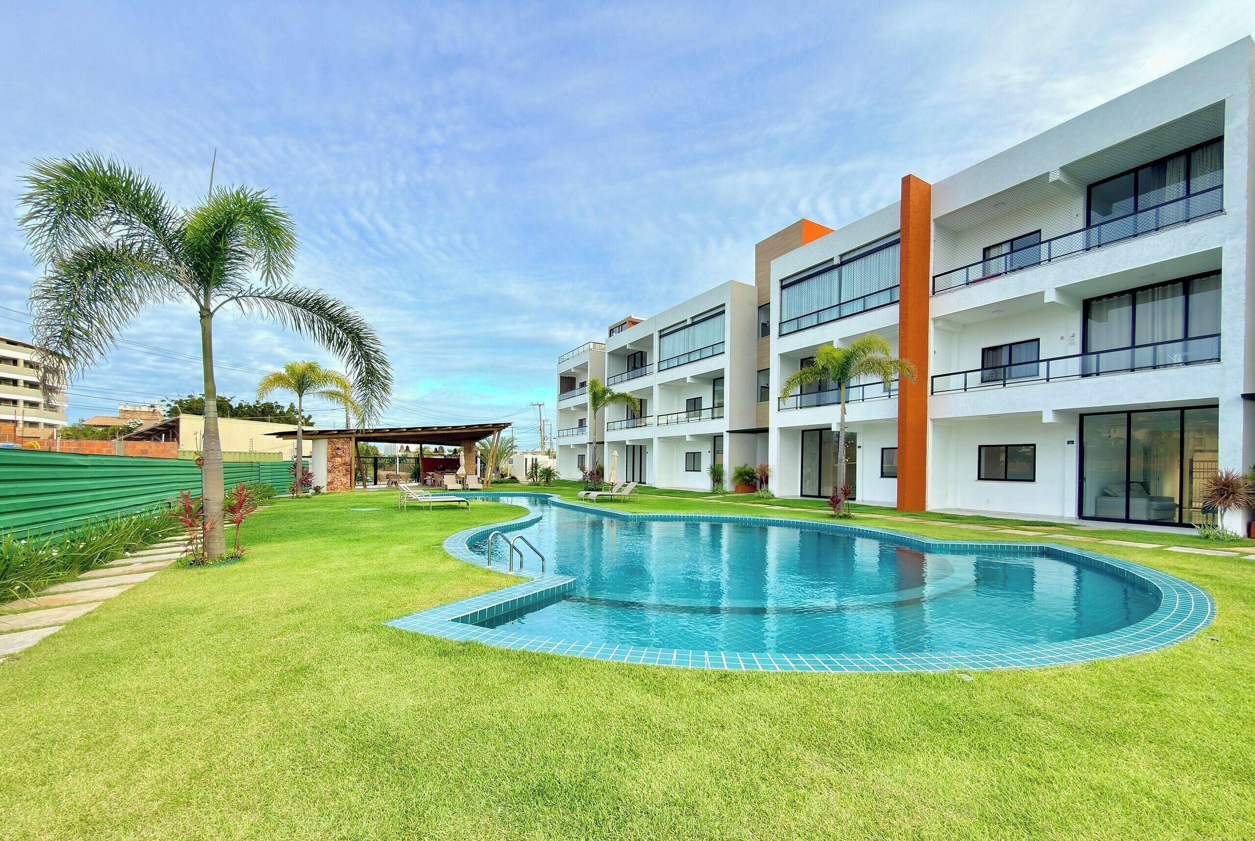 A modern hotel with a swimming pool, multiple balconies, and a well-maintained lawn.