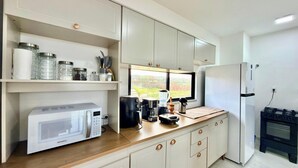 Een keuken met witte kastjes, een magnetron, een koffiezetapparaat en een koelkast.