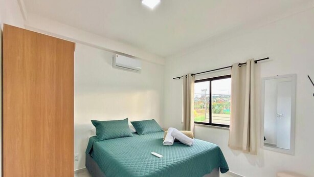 Een slaapkamer met een bed, een raam met gordijnen, een airconditioning en een deur.