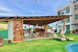 A covered outdoor area with a pool, lounge chairs, and a barbecue setup. - Bella Arte Oceanic por Be My Guest (Aquiraz)