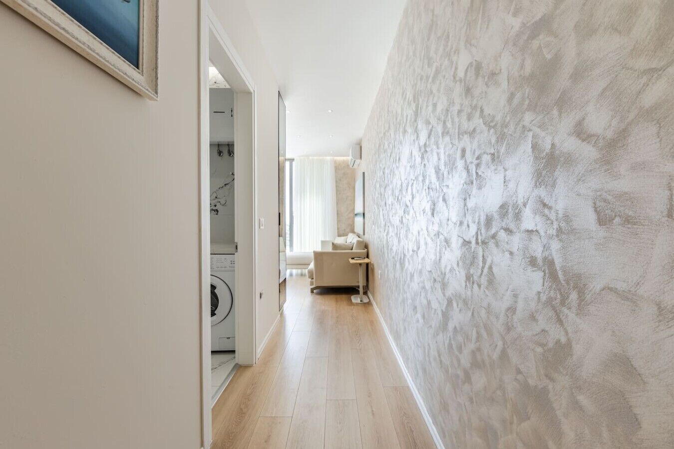 A hallway with a washing machine, a sofa, and a large textured wall.