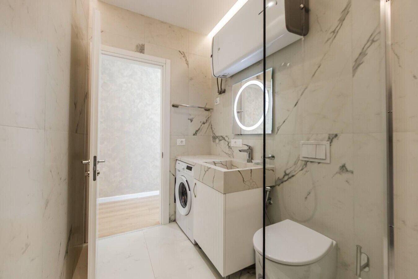 Une salle de bain moderne équipée d’un lave-linge, de toilettes et d’un lavabo avec un plan de travail en marbre.