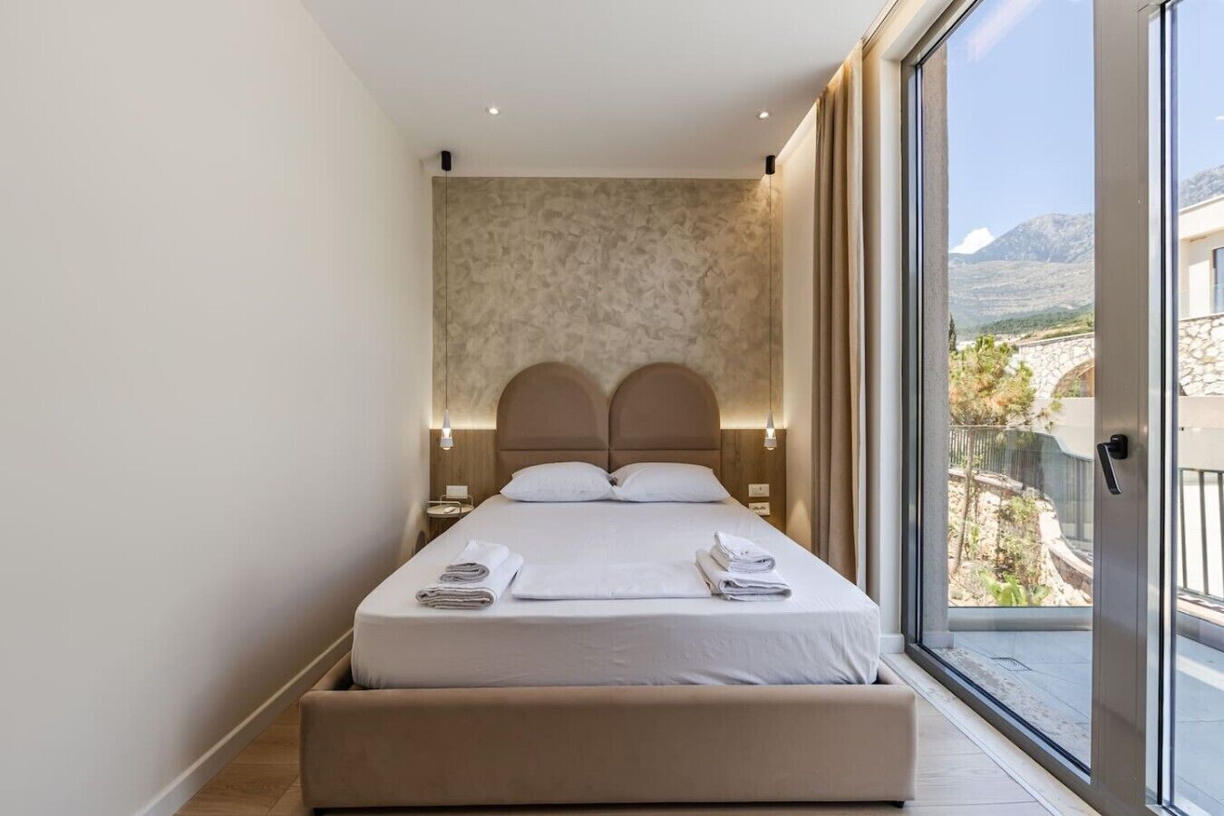 Ein modernes Hotelzimmer mit einem großen Bett, einer eingebauten Sitzbank, Blick auf eine gebirgige Landschaft und einem großen Fenster.