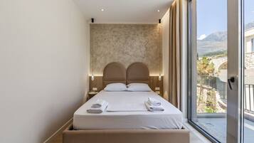 Une chambre d’hôtel moderne dotée d’un grand lit, d’une banquette intégrée, d’une vue sur un paysage montagneux et d’une grande fenêtre.