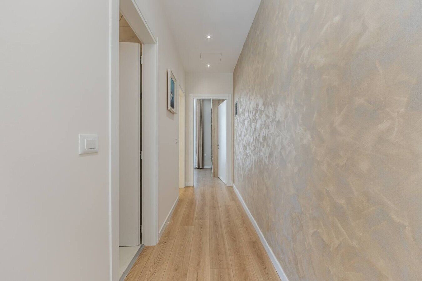 Ein Flur mit Holzboden, weißen Wänden und einer strukturierten Wand an einer Seite.