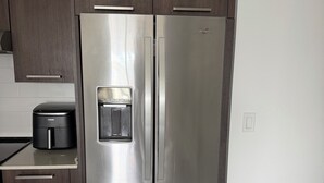 Ein Edelstahl-Kühlschrank in einer Küche mit dunklen Holzausführungen und einer weißen Arbeitsplatte.