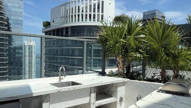 Eine Dachterrasse mit Spüle, Grill und Blick auf moderne Gebäude.