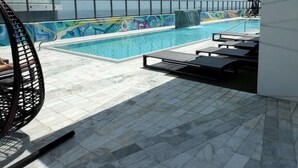 Ein Poolbereich auf dem Dach mit blauem Himmel, einem Fluchtwegweiser, einer Rutsche und Liegestühlen.