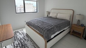 Ein Schlafzimmer mit Bett, Nachttischen, Schreibtisch, Fenster und Blick auf Gebäude.
