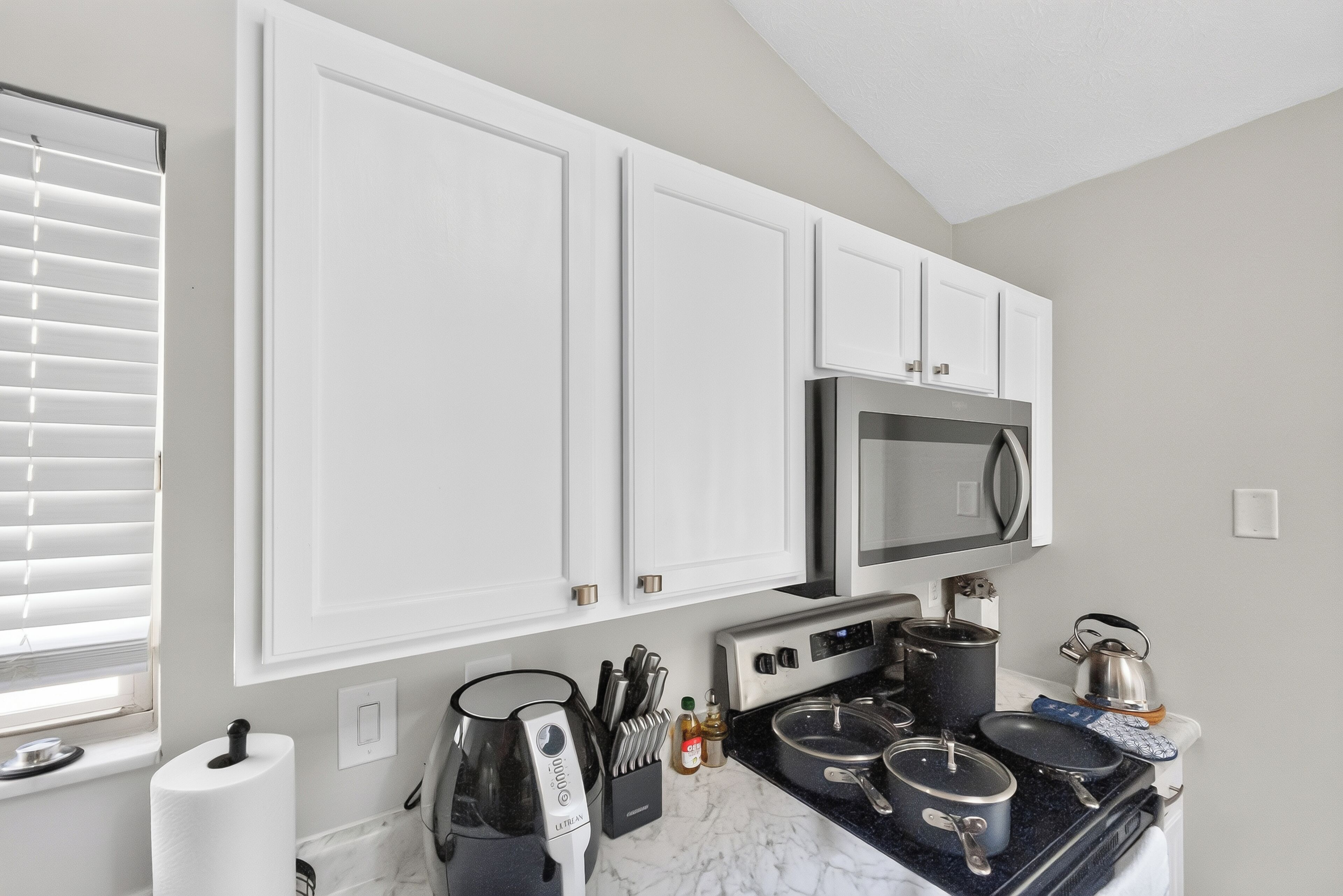 A kitchen with white cabinets, a microwave, a stove, and various cooking utensils.