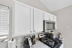 A kitchen with white cabinets, a microwave, a stove, and various cooking utensils. - Elegant 3BR 5-Bed Spacious Home: Pool & Patio (Galloway)