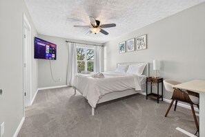 A bedroom with a bed, a desk, a chair, a ceiling fan, a TV mounted on the wall, and a window with curtains. - Elegant 3BR 5-Bed Spacious Home: Pool & Patio (Galloway)