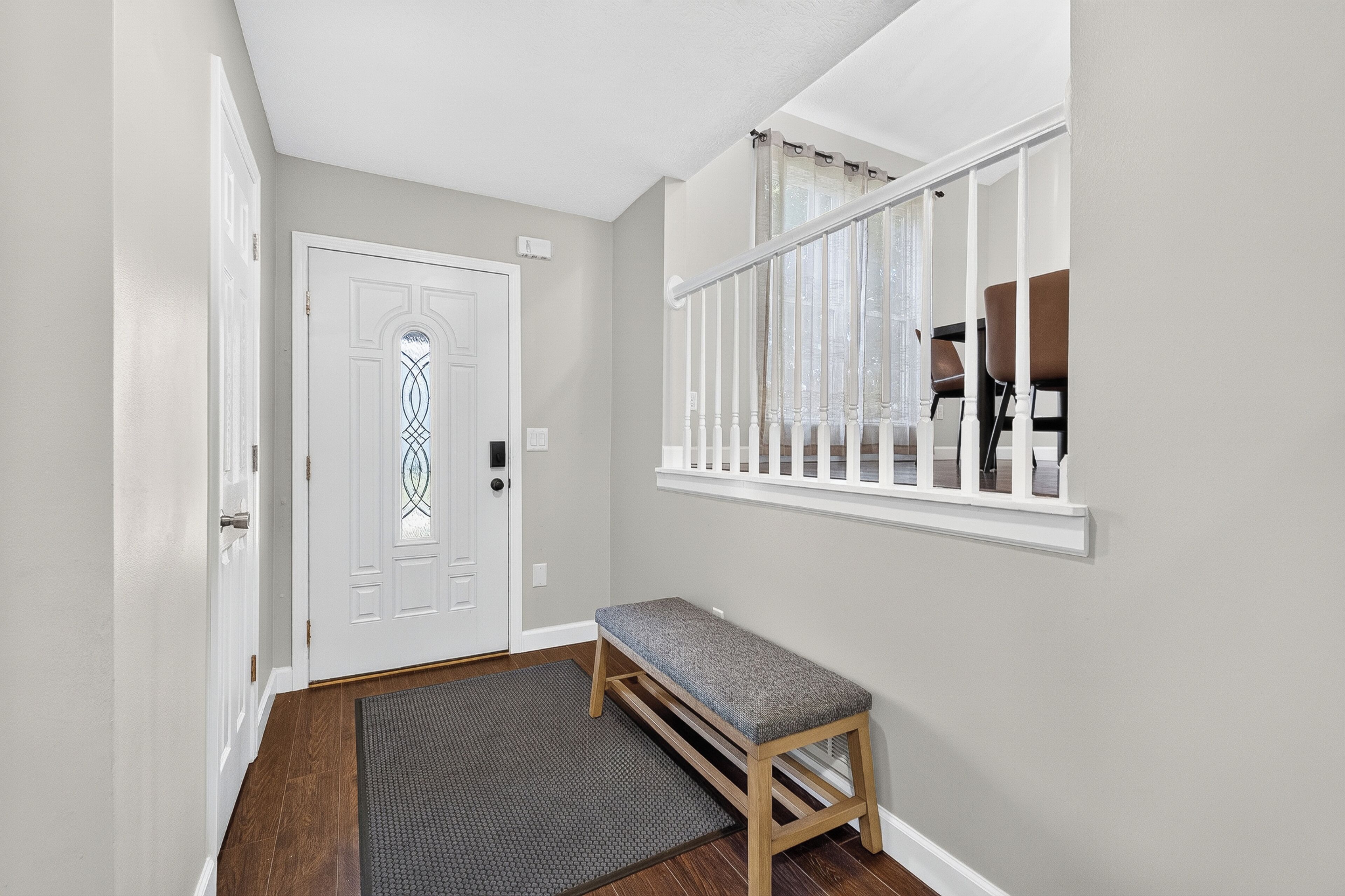 A hallway with a bench, a door, and a window with a view of chairs outside.