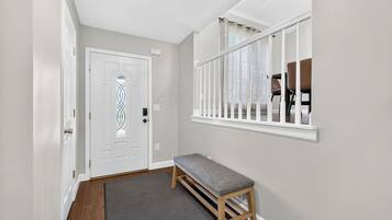 A hallway with a bench, a door, and a window with a view of chairs outside.