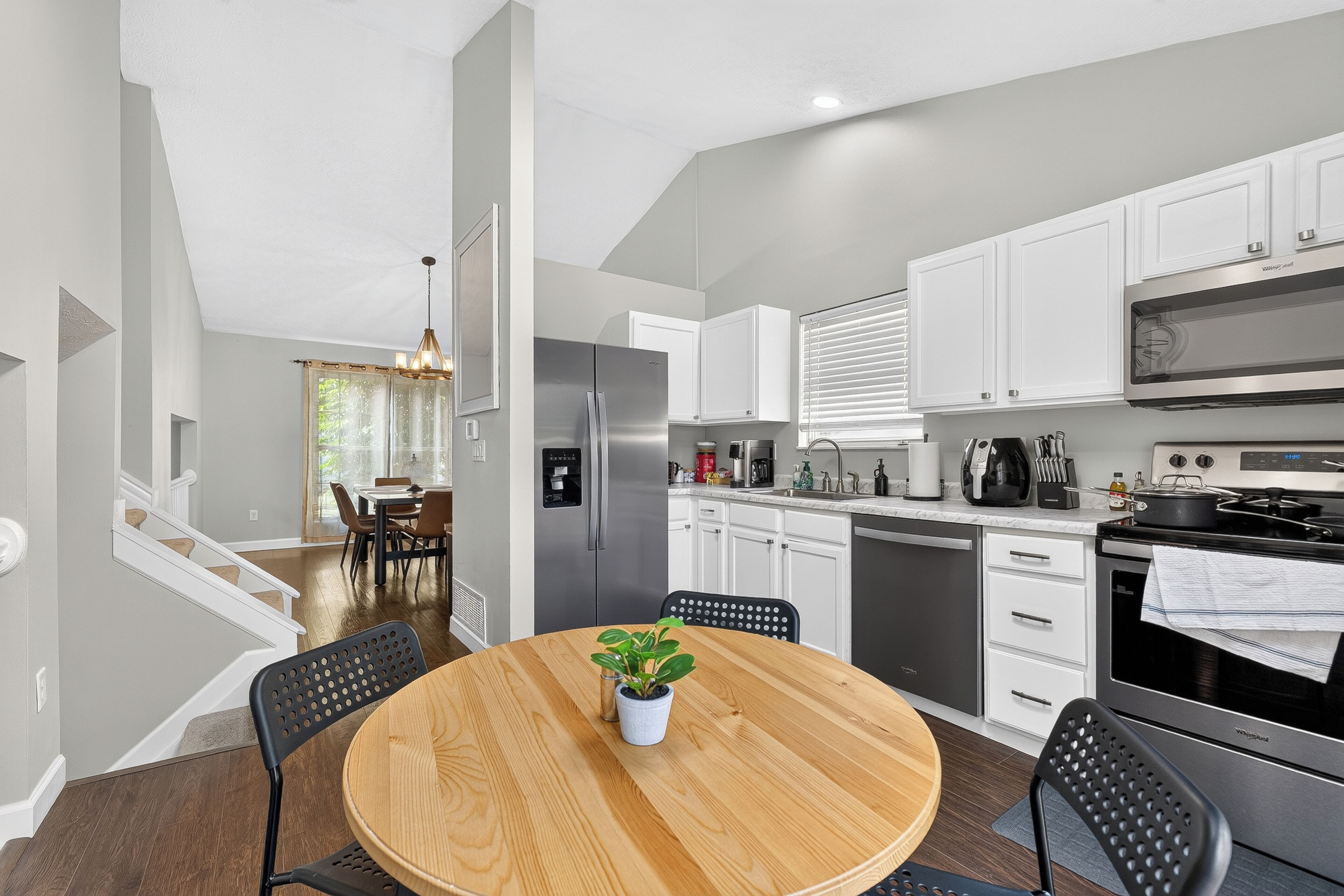A modern kitchen with white cabinets, stainless steel appliances, and a dining area with a wooden table and chairs.