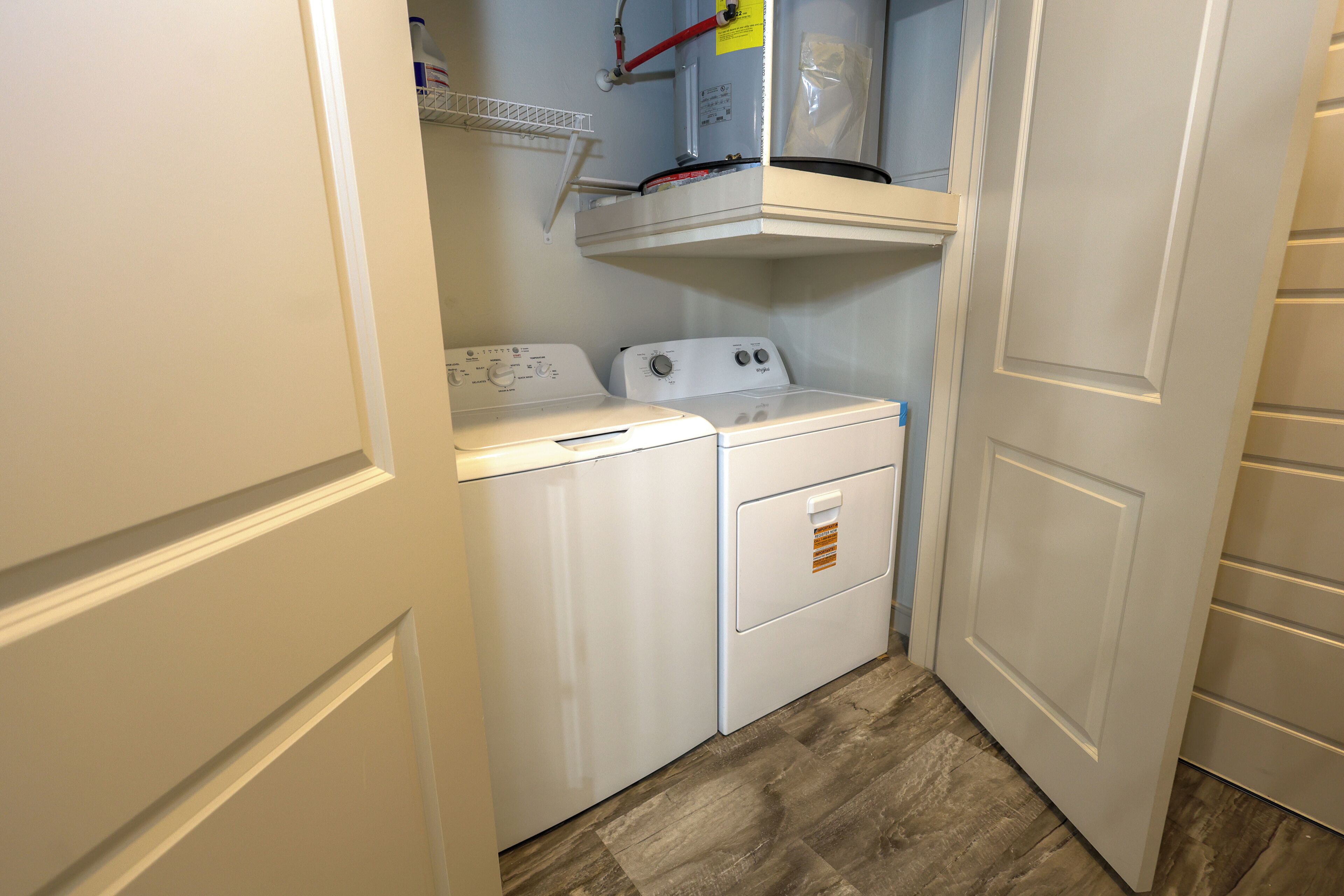 A laundry room with two white washers and dryers, a shelf above the dryers, and a wooden floor.