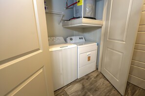 Een wasserette met twee witte wasmachines en drogers, een plank boven de drogers, en een houten vloer.