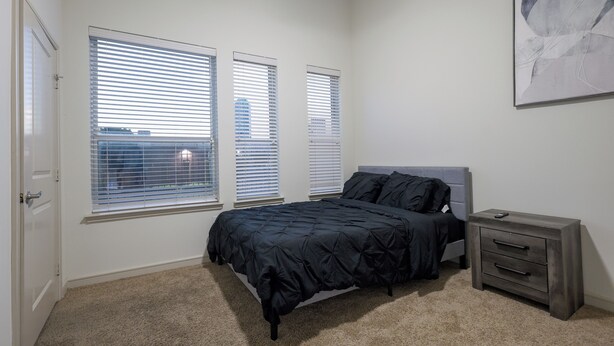 A bedroom with a bed, a nightstand, and a window with blinds. - 2-bedroom apartment in beautiful Dallas with AC and fitness room (Dallas)