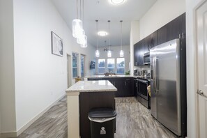 Een moderne keuken met een centraal eiland, roestvrijstalen apparatuur en hanglampen.