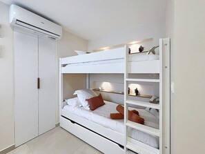 Ein Etagenbett mit weißem Kopfteil, ein Regal mit Dekoration und ein weißer Kleiderschrank.