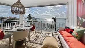 A balcony with a table set for dining, a hanging light fixture, and a sofa with cushions. - Luma, ocean view, pool, charming, central location (Grand-Case)