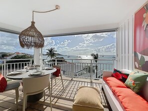 Ein Balkon mit Esstisch, einer Hängelampe und einer Couch mit Kissen.