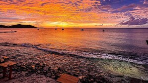 A sunset over a rocky beach with boats, a pier, and a wooden bench. - Luma, ocean view, pool, charming, central location (Grand-Case)