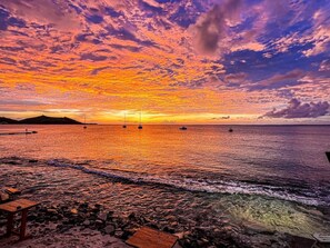 Ein Sonnenuntergang über einem felsigen Strand mit Booten, einem Steg und einer hölzernen Bank.