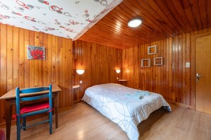 Une pièce aux murs lambrés, comprenant un lit, un bureau, une chaise et des lampes fixées au mur.