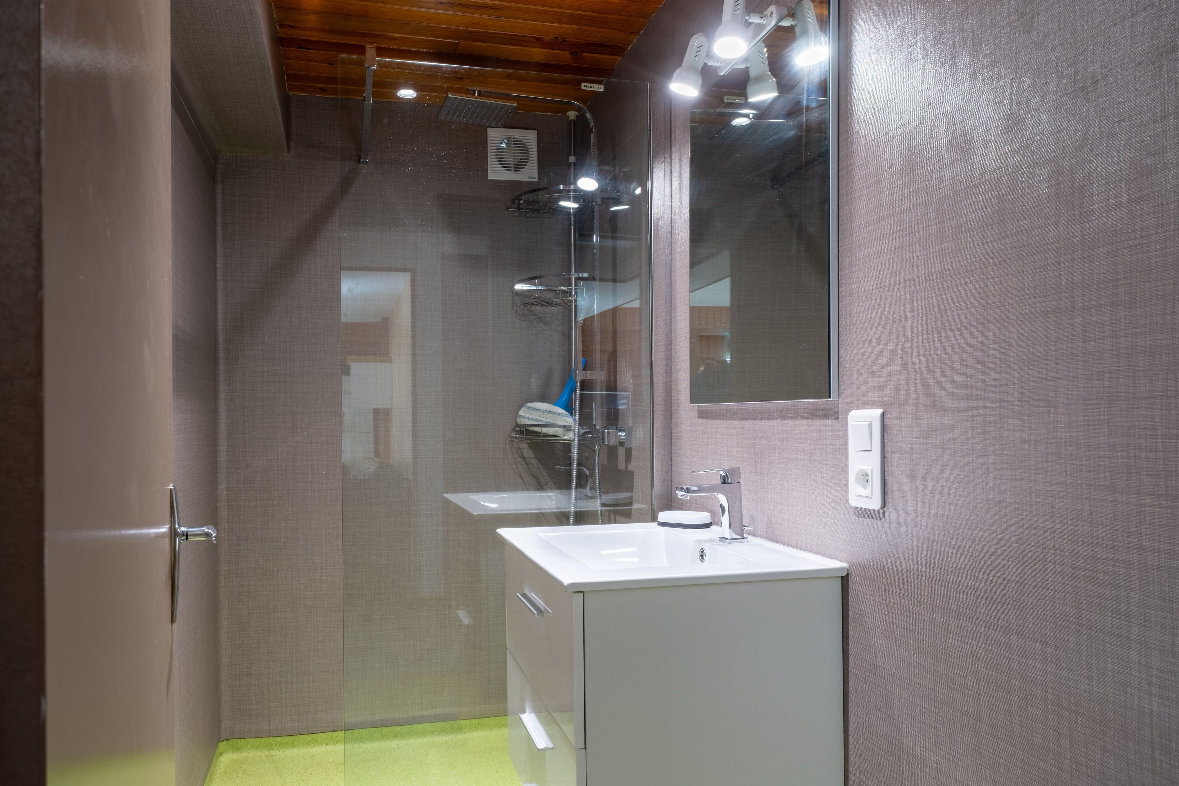 Une salle de bain moderne avec une douche à parois de verre, un lavabo blanc et un miroir au mur.