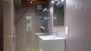 Une salle de bain moderne avec une douche à parois de verre, un lavabo blanc et un miroir au mur.