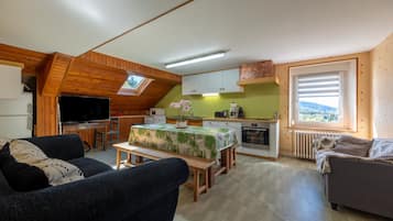 Een gezellige woonkamer met een bank en televisie, een eethoek met een tafel en stoelen, en een keuken met kasten en apparatuur.