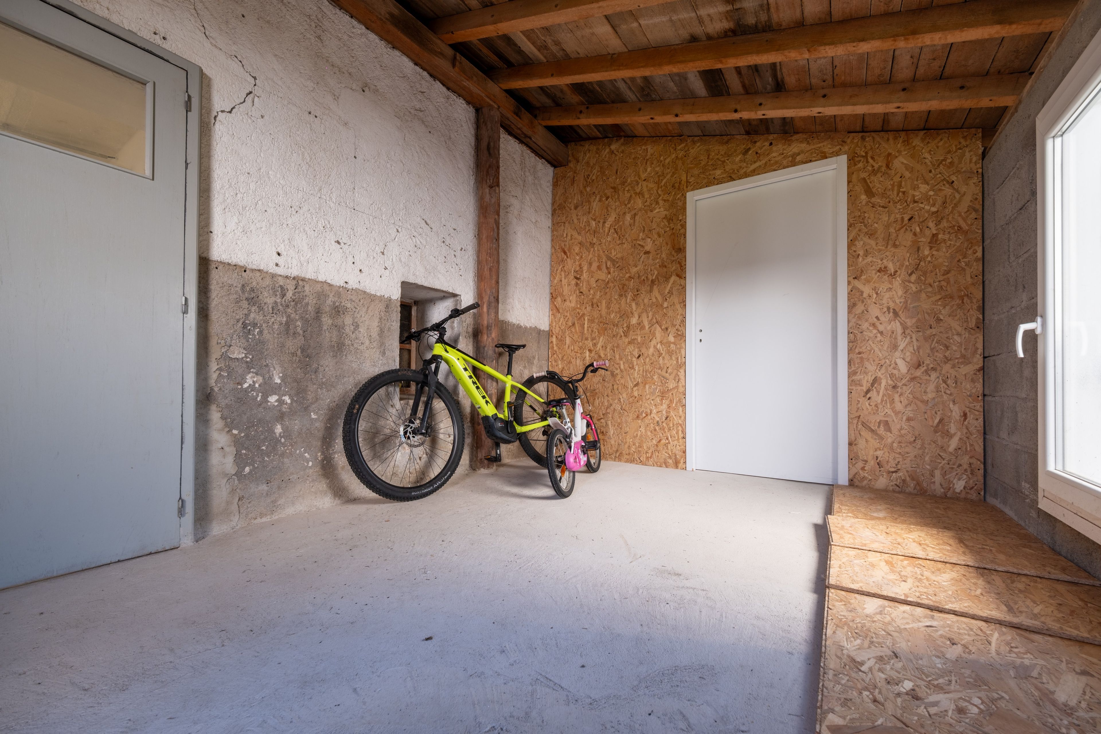 Une pièce avec un plafond en bois, une porte blanche et un vélo appuyé contre le mur.