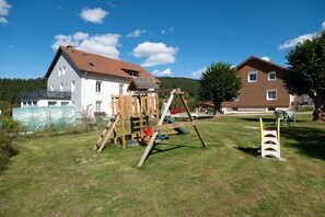 A residential area with a wooden swing set, a green play structure, and a house with a red roof.